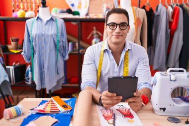 Young hispanic man tailor smiling confident using touchpad at atelier