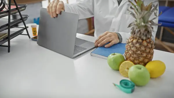 在诊所 穿着白色外套的营养师们正在关闭笔记本电脑 桌上放着水果和胶带 — 图库照片