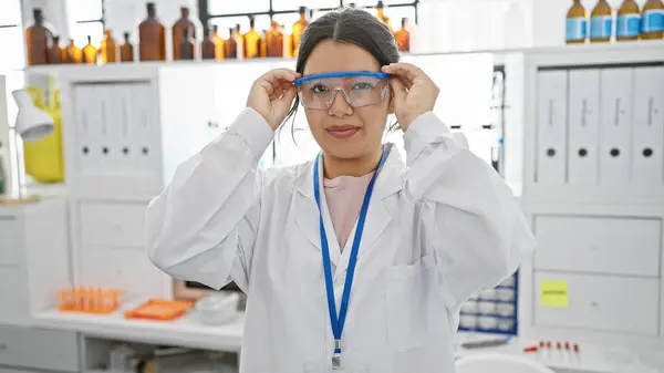 Młoda Latynoska Kobieta Dopasowuje Okulary Ochronne Laboratorium Uosabiając Profesjonalizm Badania — Zdjęcie stockowe