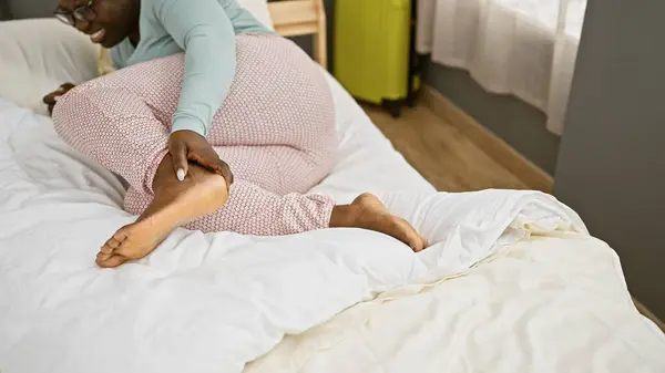 痛みの黒人女性が寝室の設定で足首を保持し 国内の怪我のシナリオを描いた — ストック写真