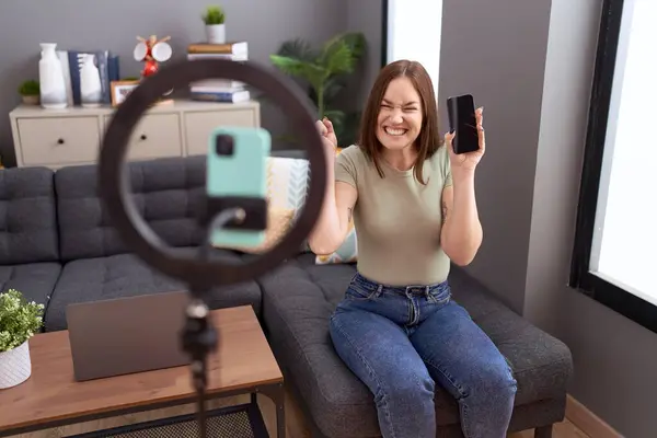 stock image Beautiful brunette woman recording vlog tutorial with smartphone at home screaming proud, celebrating victory and success very excited with raised arm 