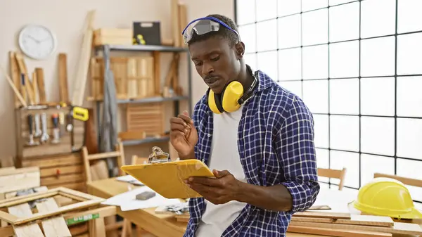 Concentrated African Man Reviews Plans Woodworking Workshop Wearing Protective Earmuffs — Stock Photo, Image