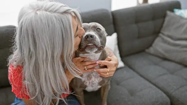 温暖的时刻 灰白头发的中年妇女和她的狗共享着一个充满爱心的吻 坐在家里的沙发上 — 图库照片