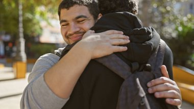 Açık şehir parkında sıcacık kucaklaşan iki adam, günlük kıyafetleri ve neşeli tavırlarıyla açıkça görünen bir arkadaşlık..