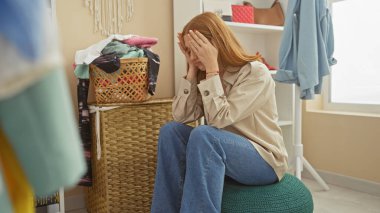 Sıkıntılı genç bir kadın dağınık bir soyunma odasında oturuyor ve elleriyle yüzünü örtüyor..