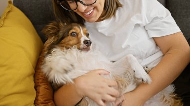 Latin bir kadın, rahat bir oturma odasında köpeğe sarılıyor. Arkadaşlık ve konfor tasvir ediyor..