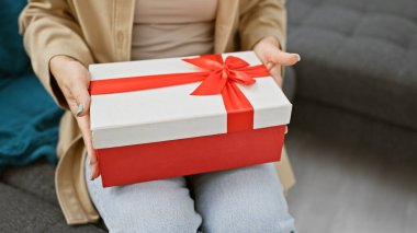 Evde, rahat bir ortam, rahat bir koltukta oturan bir kadını sarar. Elleri nazikçe bir hediye tutar ve sıradan bir oturma odasına cazibe katar.