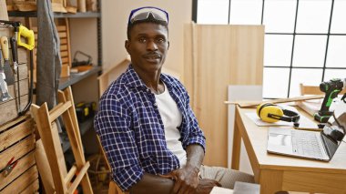 Afrikalı Amerikalı bir adam iyi donanımlı bir marangozluk atölyesinde güvenle poz veriyor..