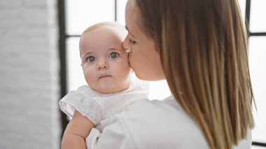 Rahat ve rahat, bir anne ayakta duruyor, sevgi dolu bir şekilde kızını kollarına alıyor, gerçek aşkını yumuşak bir öpücükle ifade ediyor..
