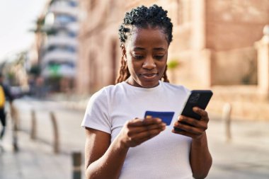 African american woman using smartphone and credit card at street