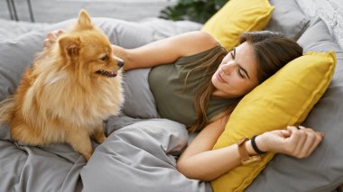 Neşeli genç İspanyol kadın kendine güveni yayıyor, gülüyor ve köpeğiyle eğleniyor, dairesinde yatağında uzanıyor..