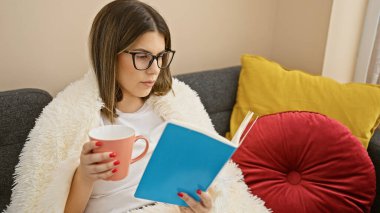 Genç bir İspanyol kadın evinde rahatlıyor, bir kitapla meşgul olurken rahat bir kanepede kahve fincanından yudumluyor..