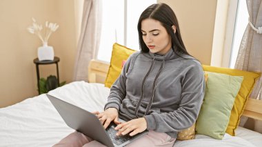 Odaklanmış İspanyol bir kadın, rahat bir yatak odası ortamında dizüstü bilgisayarıyla çalışıyor, evde verimlilik ve rahatlık gösteriyor..