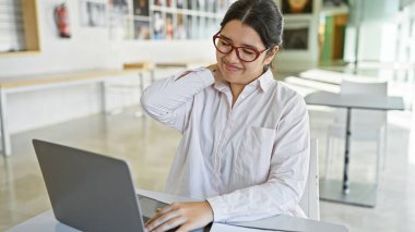 Modern ofis işyerinde boynu ağrıyan gözlüklü İspanyol genç bir kadın.