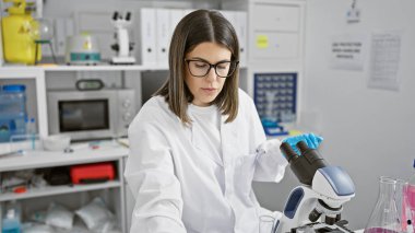 İspanyol kadın bilim adamı laboratuvar ortamında mikroskopla örnekleri analiz ediyor.