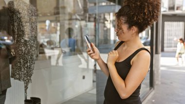 Kıvırcık saçlı, şehirde akıllı telefon kullanan genç İspanyol kadın..
