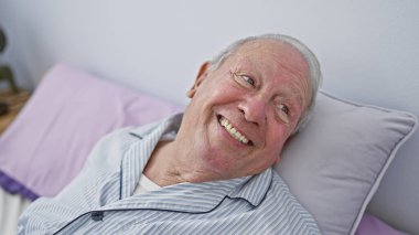 Kendinden emin, yürek ısıtan bir gülümsemesi olan, rahat yatak odasının samimi atmosferinde sıcak bir sabahın tadını çıkaran kıdemli bir adam..