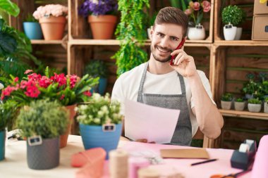 Genç beyaz erkek çiçekçi çiçekçide akıllı telefondan kitap okuyor.