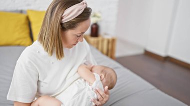 Kendini işine adamış bir anne, evde rahat bir yatak odasında oturup bebeğini sevgiyle emzirirken konsantrasyonunu gösteriyor. Atletik ev bakımı yaşam tarzını ciddiyetle bağrına basmak..