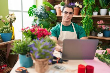 Young hispanic man florist smiling confident using laptop at flower shop