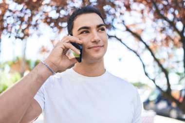 Genç İspanyol adam gülümsüyor. Parktaki akıllı telefondan konuşuyor.