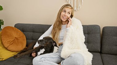 Genç, güzel bir kadın, köpeğiyle birlikte gri bir koltukta otururken telefonda konuşuyor, rahat, rahat bir atmosfer yayıyor..