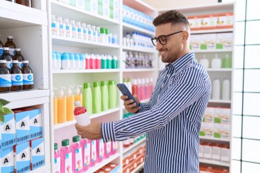 Young hispanic man customer make photo by smartphone to medicine bottle at pharmacy