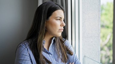 Genç, güzel, İspanyol bir kadın evde üzgün bir ifadeyle pencereden dışarı bakıyor.