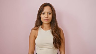 Havalı ve rahat, çekici bir saç stili ve ciddi bir ifadeye sahip, pembe arka planda izole bir şekilde kameraya bakan genç, güzel İspanyol bir kadın..