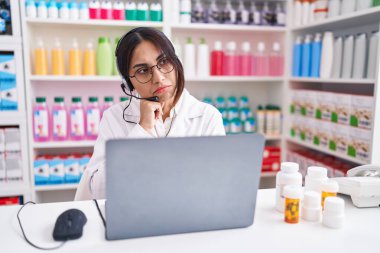 Eczanede çalışan genç Arap kadın elleri çenesinde dizüstü bilgisayar kullanarak soru sormayı, düşünceli ifadeyi düşünüyor. Düşünceli bir yüzle gülümsüyor. şüphe kavramı. 