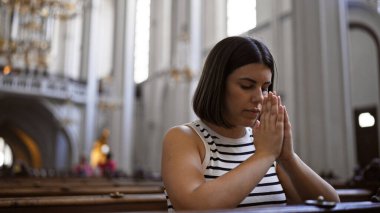 Young beautiful hispanic woman praying on a church bench at Augustinian Church in Vienna clipart