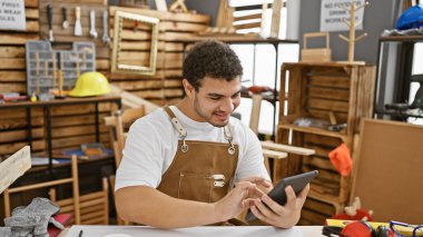 İçerideki bir marangoz atölyesinde tablet kullanan gülümseyen bir adam.