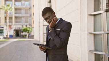 Sokakta tablet kullanan takım elbiseli Afro-Amerikan bir adam..