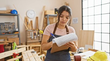 Genç bir İspanyol kadın, iyi donanımlı bir marangozluk atölyesinde planlarını gözden geçiriyor..