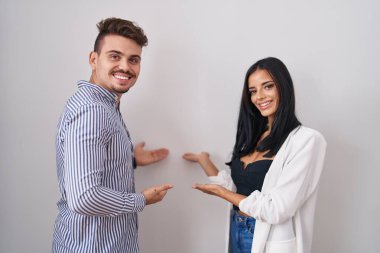 Young hispanic couple standing over white background inviting to enter smiling natural with open hand 