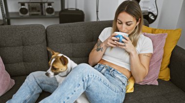 Genç bir kadın evinde köpeğiyle huzurlu bir anın tadını çıkarıyor, rahat bir kanepede kahve yudumluyor..