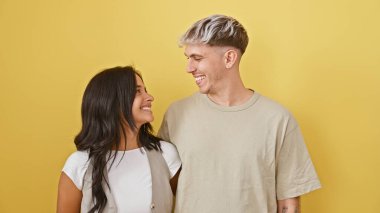 Sevgi dolu bir çift birbirine sıcak bir şekilde gülümser. Parlak sarı bir arkaplan karşısında. Sevginin güzel bir anını tasvir ederler..