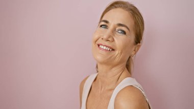 Gülümseyen beyaz, olgun bir kadın pembe izole bir arka plana poz veriyor, kendine güven ve güzellik yayıyor..