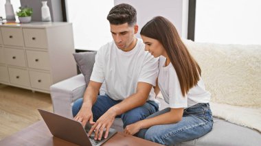 Bir çift evlerinin oturma odasındaki dizüstü bilgisayarda modern ev hayatını sembolize ederek içeriği keşfediyor..