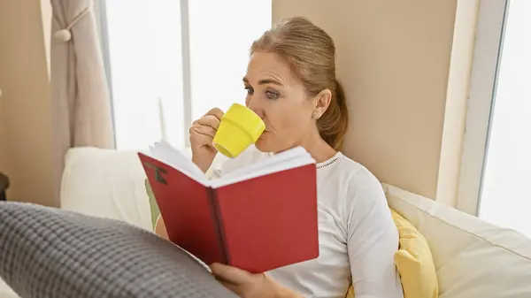 Dospělá Žena Odpočívá Doma Upíjí Žlutého Hrnku Čte Červenou Knihu — Stock fotografie