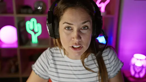 一个全神贯注的女人 带着耳机 在一个五颜六色的游戏房间里 凝视着屏幕 — 图库照片