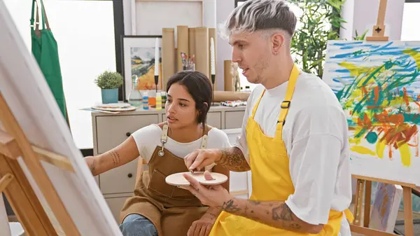 stock image A man and woman in aprons collaborating on a colorful abstract painting in an art studio.