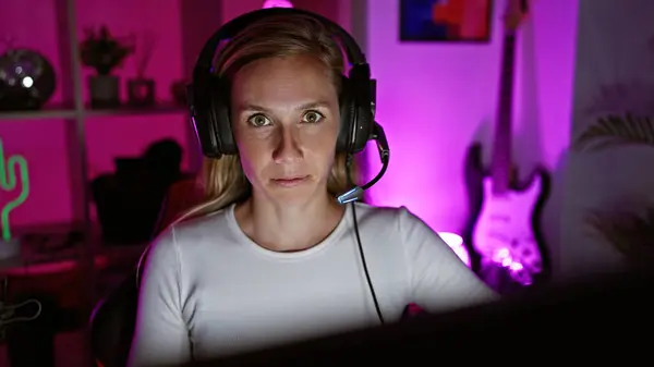 在一个充满活力的粉色灯火通明的游戏室里 一个专心致志的金发女人戴着耳机 — 图库照片