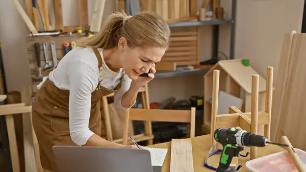 Blonde Woman Multitasking Carpentry Workshop While Talking Phone Writing Notes — Stock Photo, Image
