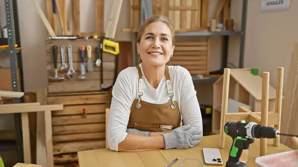 Smiling caucasian woman wearing an apron in a woodworking workshop with tools and workbench