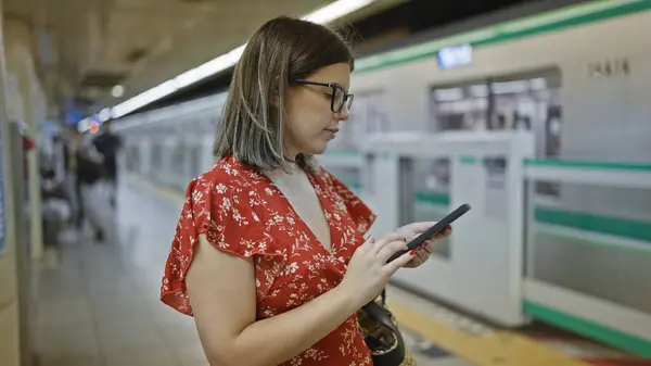 陽気な若いヒスパニック系女性は スマートフォンにメッセージを入力しながら 賑やかな都市駅で地下鉄の電車を辛抱強く待って 新しい旅に出ました — ストック写真