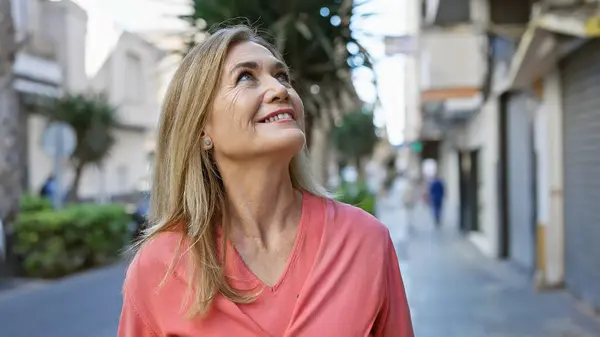 Uśmiechnięta Blondynka Średnim Wieku Spogląda Górę Spacerując Ulicach Miasta Emanując — Zdjęcie stockowe