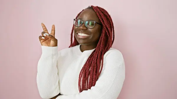 一个戴着辫子 面带微笑的非洲裔美国女人的画像 在粉色背景上做一个和平标志 — 图库照片