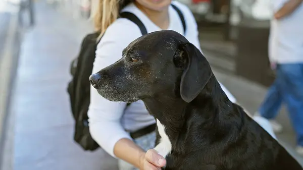 A young woman pets her black labrador on a bustling urban street, portraying a moment of connection amid the city bustle.
