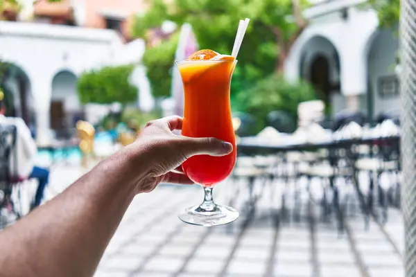 Man Hand Holds Vibrant Cocktail Blurred Patio Background Exemplifying Leisure — Stock Photo, Image